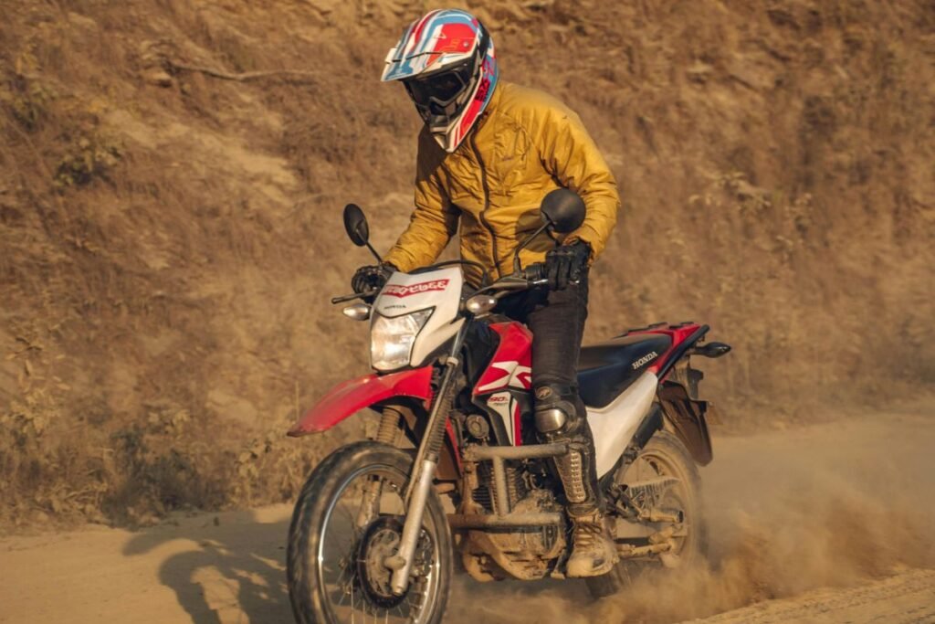 "A motorcyclist riding a red and white Honda dirt bike on a dusty off-road trail in Nepal, wearing a yellow jacket, helmet, and protective gear"